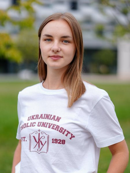 Porträt-Foto von Anna Sobolevska. Die junge Frau hat lange, glatte blonde Haare und trägt ein weißes T-Shirt der Ukrainischen Katholischen Universität Lwiw.