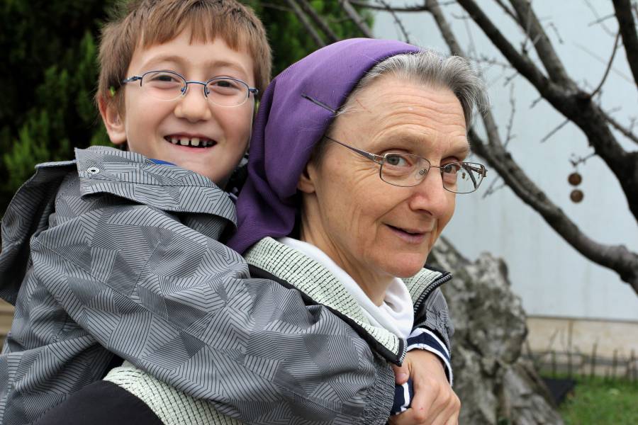 Ordensfrau trägt einen Jungen auf dem Rücken.