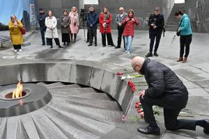 Das Bild zeigt am rechten Rand Pfarrer Thomas Schwartz, der vor der Flamme an der Gedenkstätte niederkniet und eine Blume ablegt.