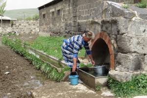 Eine Frau füllt am Dorfbrunnen zwei Eimer mit Trinkwasser.