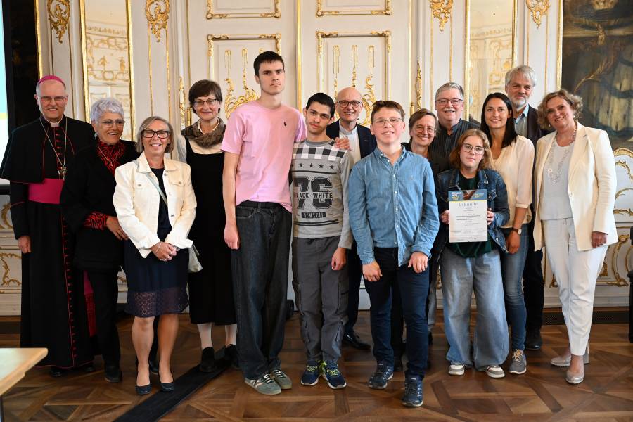 Die Preisträgerinnen und -träger des ersten Preises - dotiert mit 1000 Euro - beim Gruppenfoto mit den Vertreterinnen und Vertretern des Bistums Augsburg, von Renovabis und der Regierung von Schwaben. Sie stehen gemeinsam im Rokokosaal der Regierung von Schwaben.