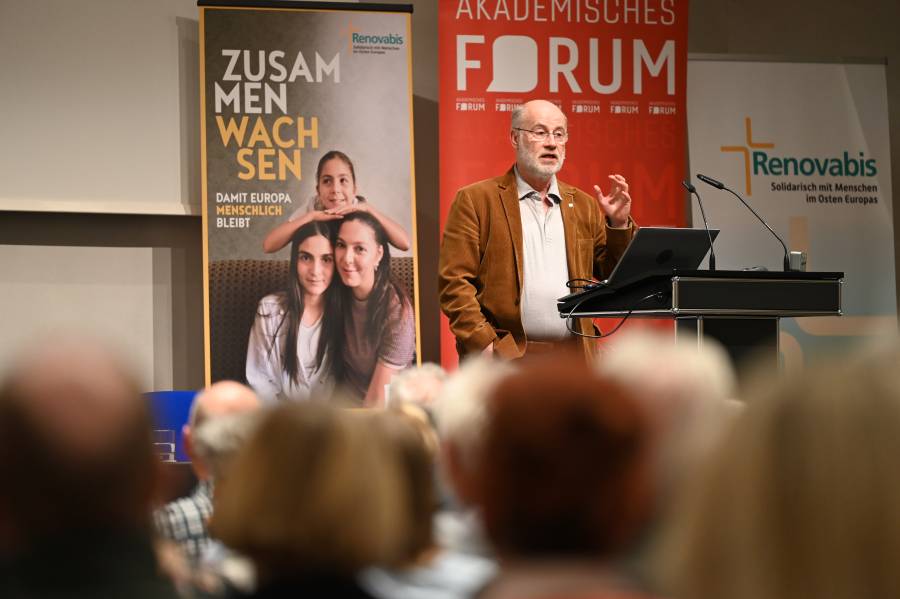 Prof. Harald Lesch auf der Bühne vor dem Plakat zur Renovabis-Pfingstaktion, einem Roll-up von Renovabis und einem des Akademischen Forums Augsburg.