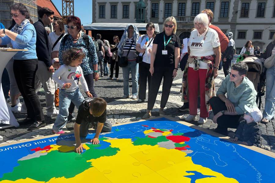 Auf dem Boden liegt das riesige Renovabis-Puzzle mit den 29 Partnerländern des Hilfswerks. Auf den knallbunten Flächen knien Kinder, die versuchen, das Puzzle richtig zusammenzusetzen, daneben steht die Bundestagsabgeordnete Claudia Roth.
