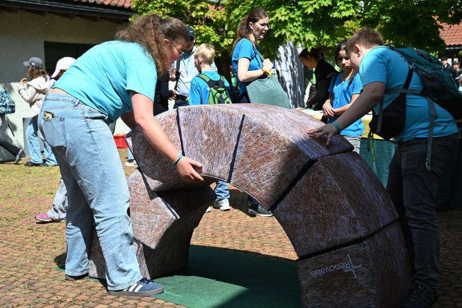 Eine Frau in Jeans und ein blauem T-Shirt sowie ein Junge beim Zusammensetzen der Renovabis-Brücke im strahlenden Sonnenschein.
