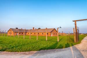 Backsteinbaracke hinter einem Stacheldrahtzaun auf dem Gelände von Auschwitz-Birkenau, morgens bei Sonnenschein.