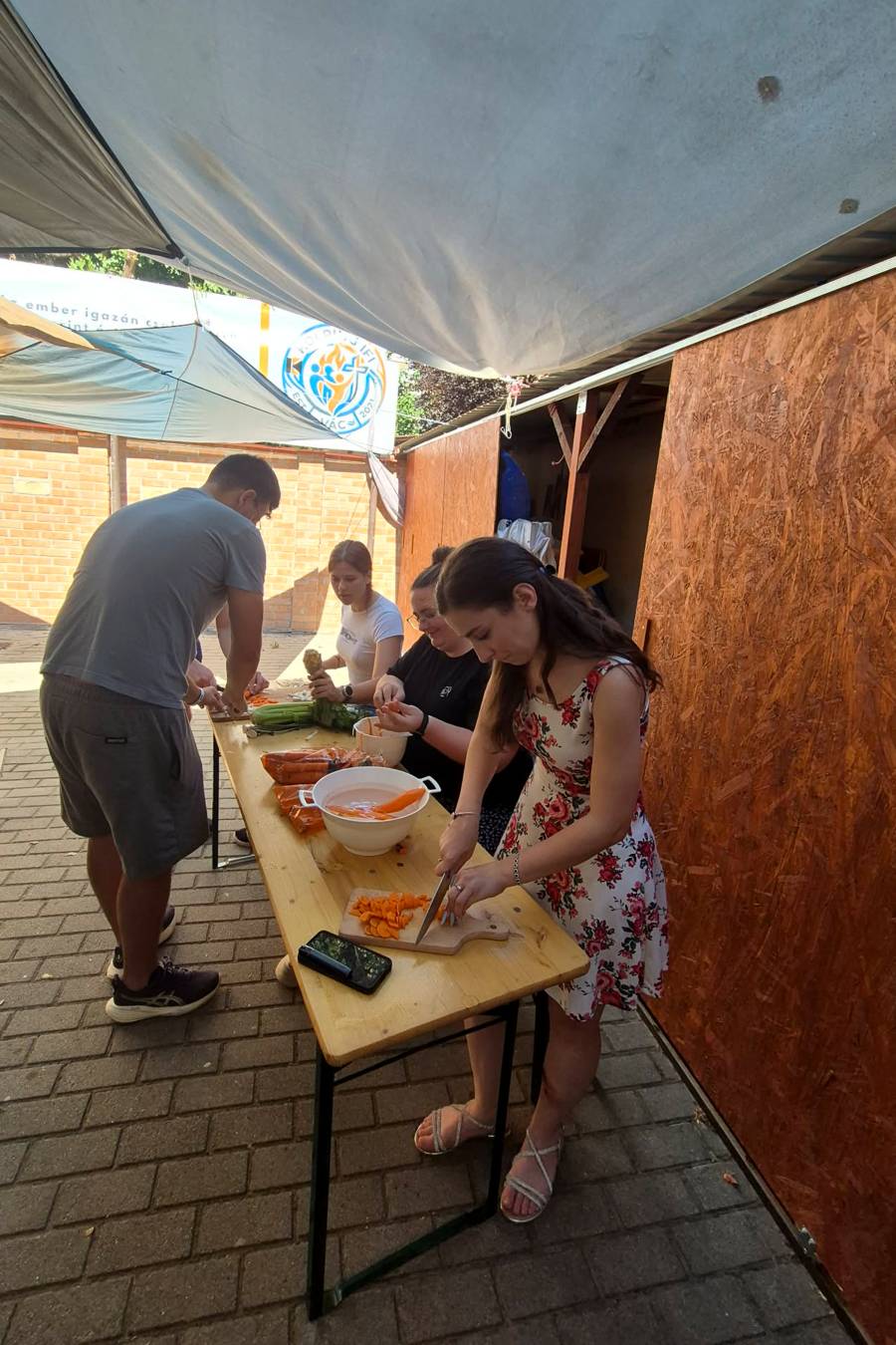Junge Frauen und Männer stehen in Sommerkleidung an einem Biertisch und schneiden Gemüse.