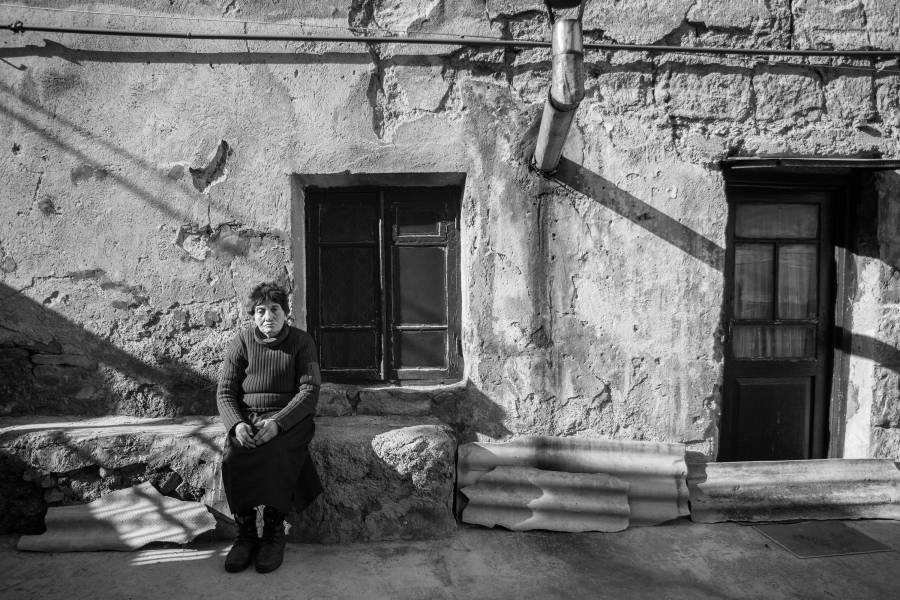 Schwarzweiß-Foto von einer Frau auf einer Bank vor ihrem Haus im Norden Armeniens