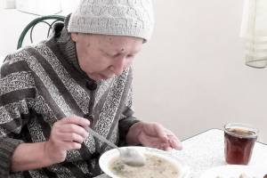 Eine ältere Frau isst einen Teller Suppe.