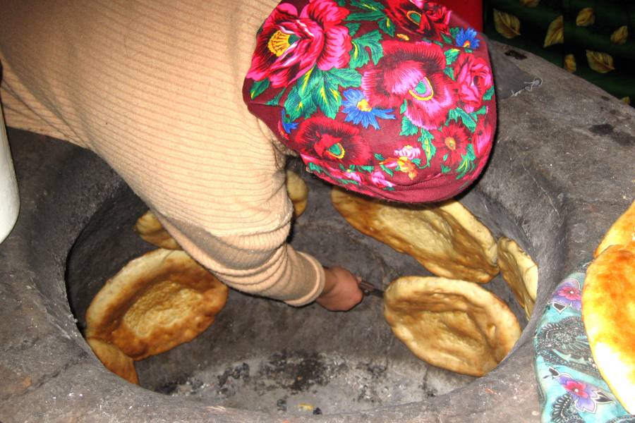 Frau beim Brotbacken in einem Erdofen
