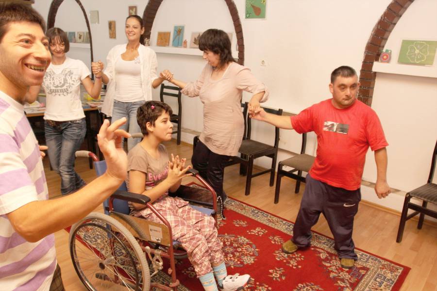 Mädchen im Rollstuhl, eine Gruppe Menschen tanzt um sie herum